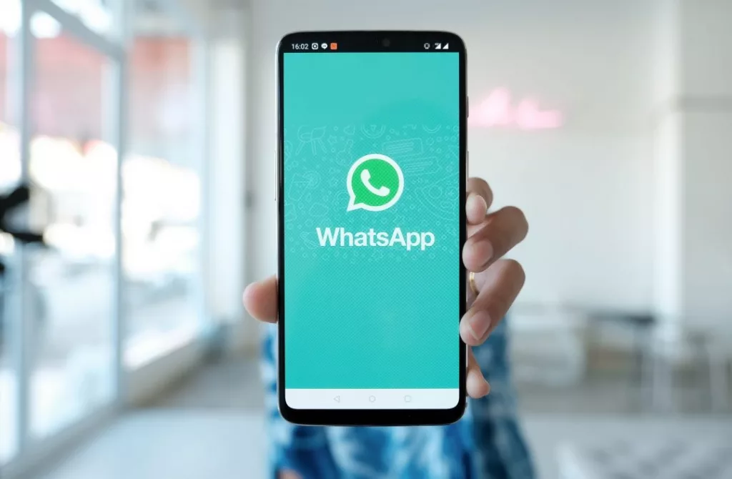 homem no fundo segurando o celular com o símbolo do WhatsApp na tela